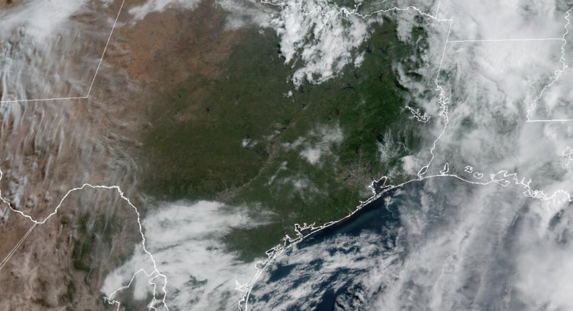 Vista del horizonte de Houston bajo un cielo parcialmente nublado y soleado con una capa de neblina visible en el ambiente, representando un Día de Acción por Ozono con calidad del aire poco saludable y altas temperaturas veraniegas en la ciudad.