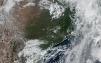 Vista del horizonte de Houston bajo un cielo parcialmente nublado y soleado con una capa de neblina visible en el ambiente, representando un Día de Acción por Ozono con calidad del aire poco saludable y altas temperaturas veraniegas en la ciudad.