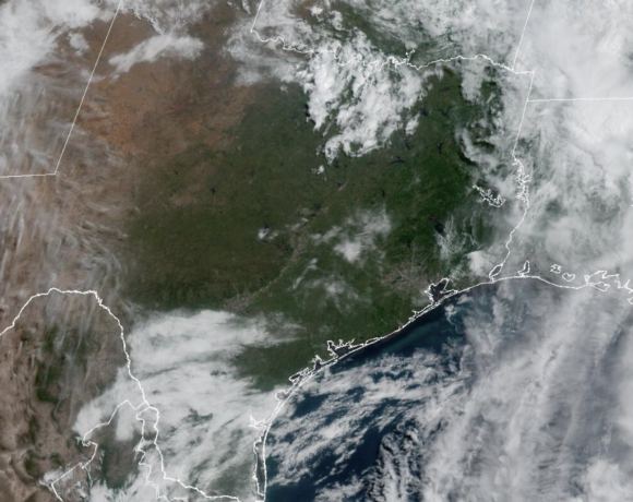 Vista del horizonte de Houston bajo un cielo parcialmente nublado y soleado con una capa de neblina visible en el ambiente, representando un Día de Acción por Ozono con calidad del aire poco saludable y altas temperaturas veraniegas en la ciudad.