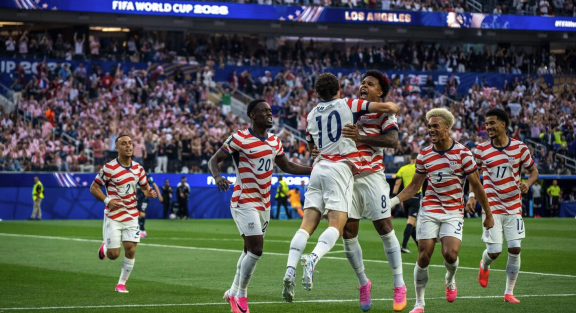os jugadores de la selección masculina de Estados Unidos celebran uno de sus cuatro goles ante Paraguay en el SoFi Stadium de Inglewood, California, durante su debut en el Mundial 2026, rodeados de miles de aficionados con banderas americanas.