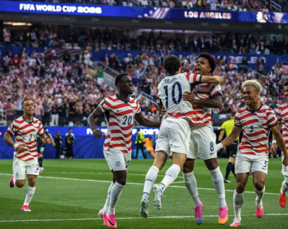 os jugadores de la selección masculina de Estados Unidos celebran uno de sus cuatro goles ante Paraguay en el SoFi Stadium de Inglewood, California, durante su debut en el Mundial 2026, rodeados de miles de aficionados con banderas americanas.